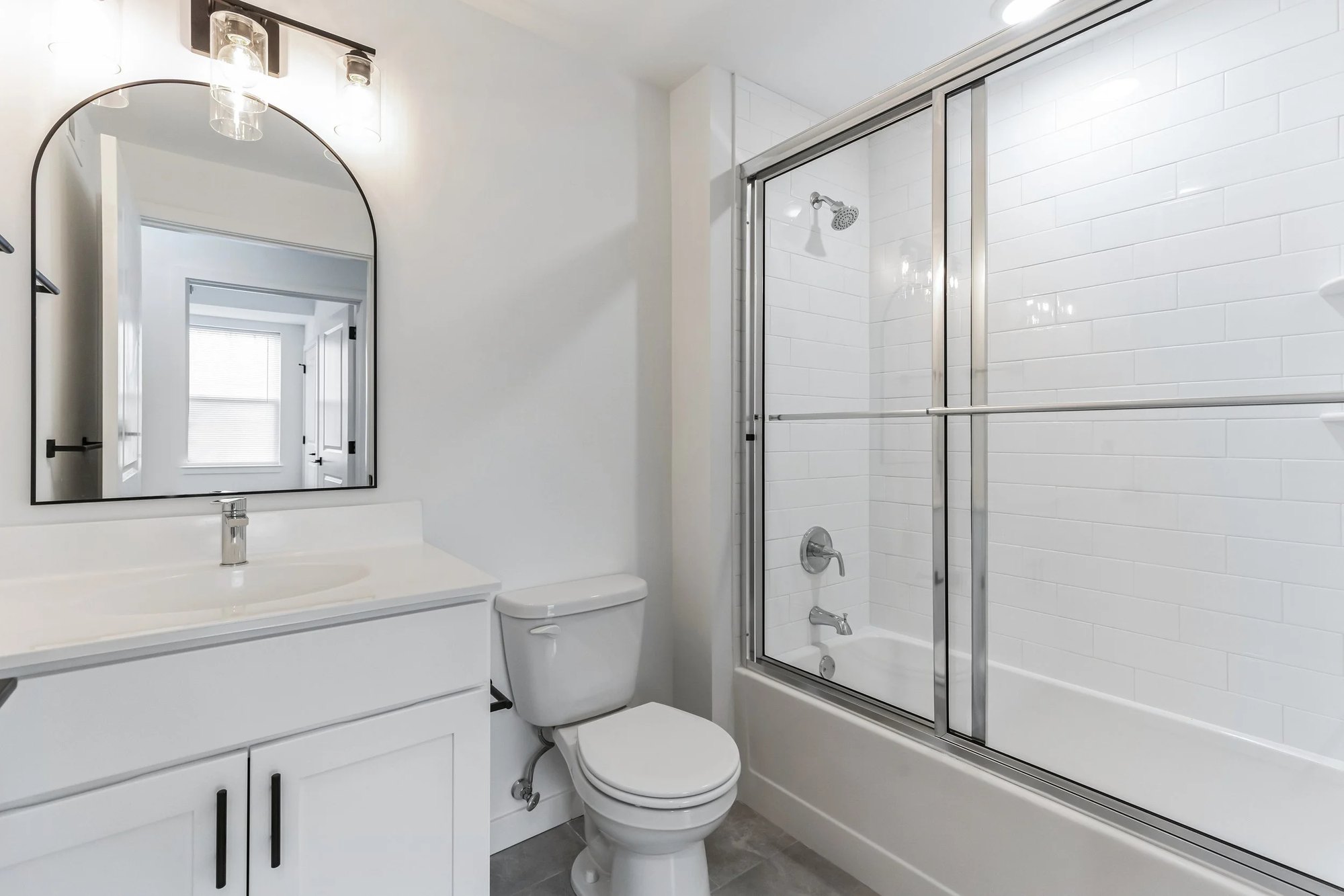 Full bathroom with vanity, arched mirror, and tub-shower combination