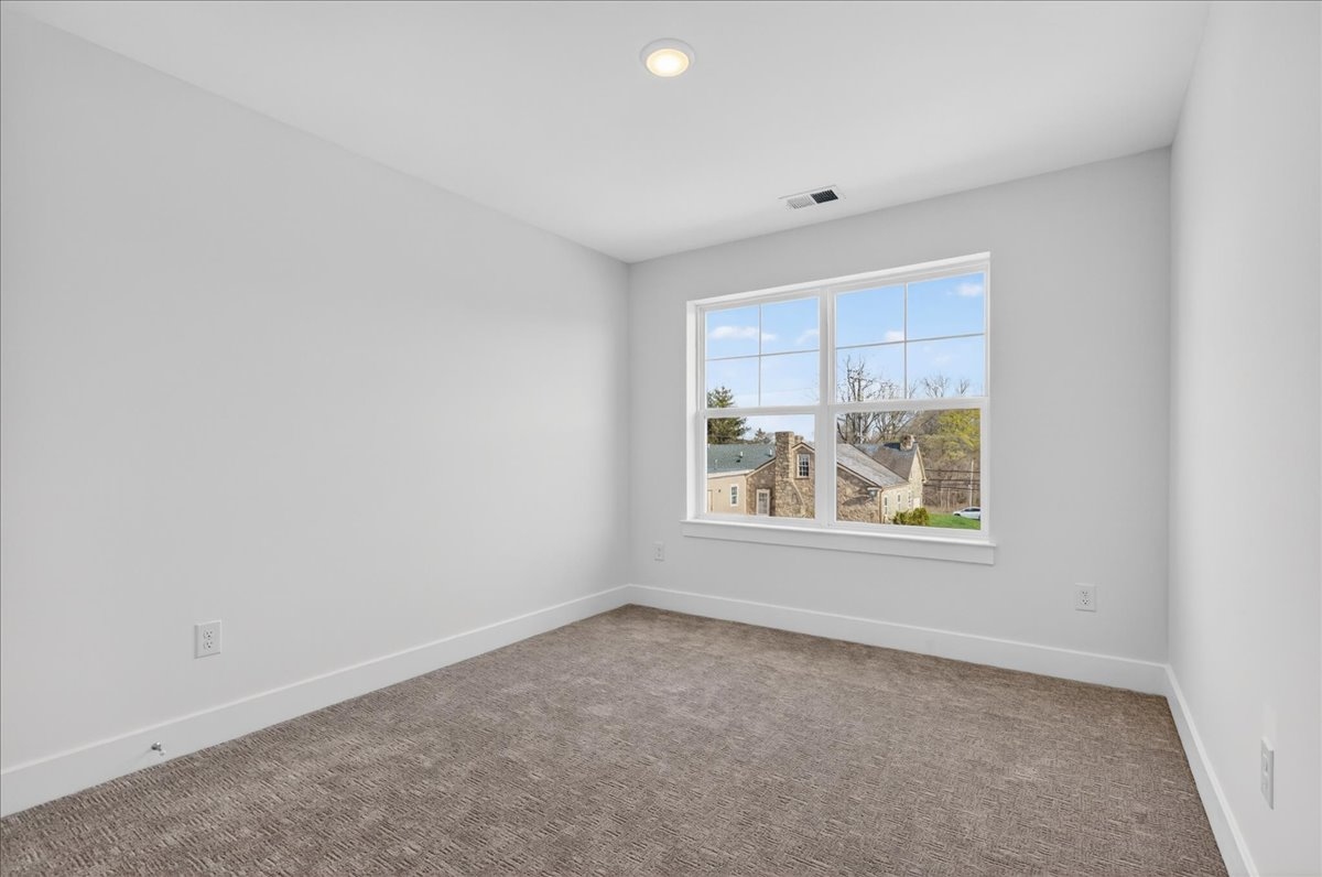 Secondary bedroom with a corner window looking out to a nearby stone home and mature trees