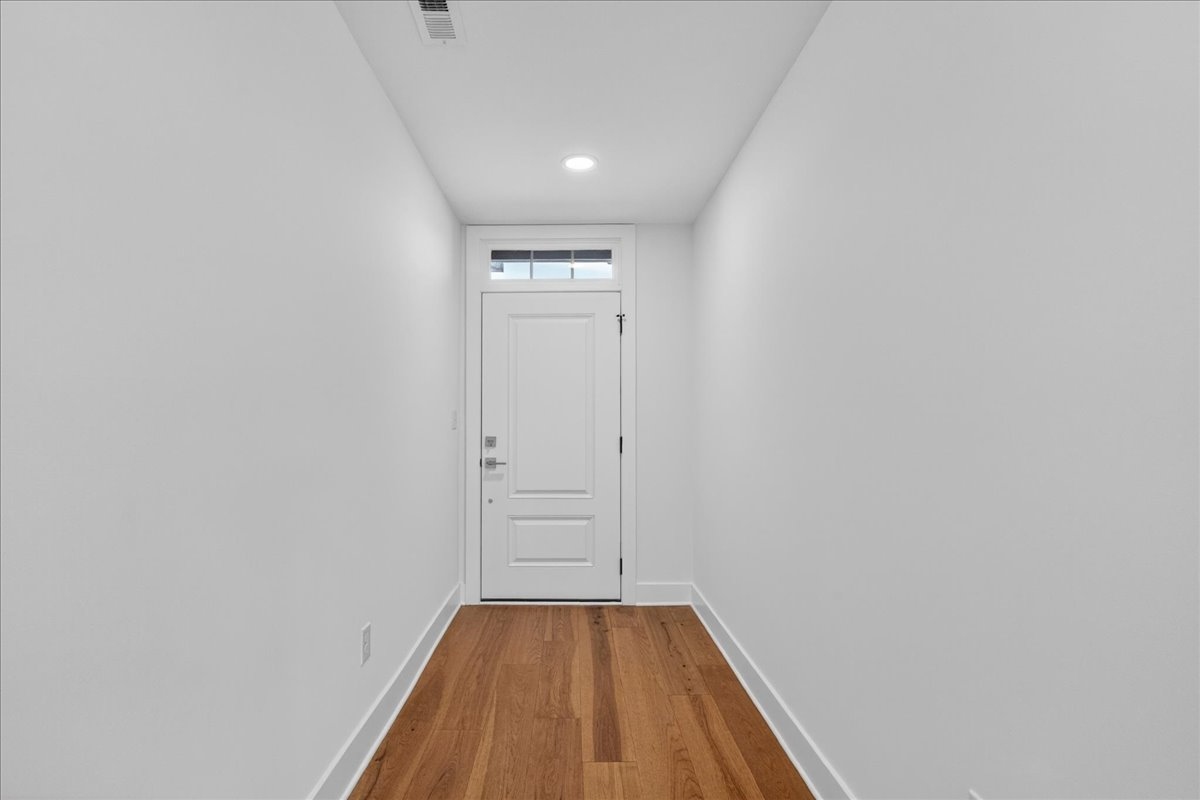 Entry foyer with hardwood flooring and a white paneled front door with transom window