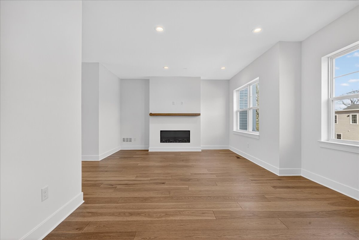 Family room with a linear electric fireplace, floating wood mantel, and double windows