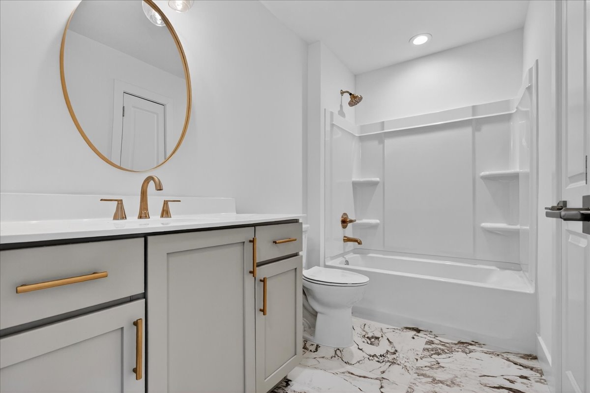 Secondary bath alternate view showing gray shaker double vanity, brass fixtures, and glass-enclosed shower