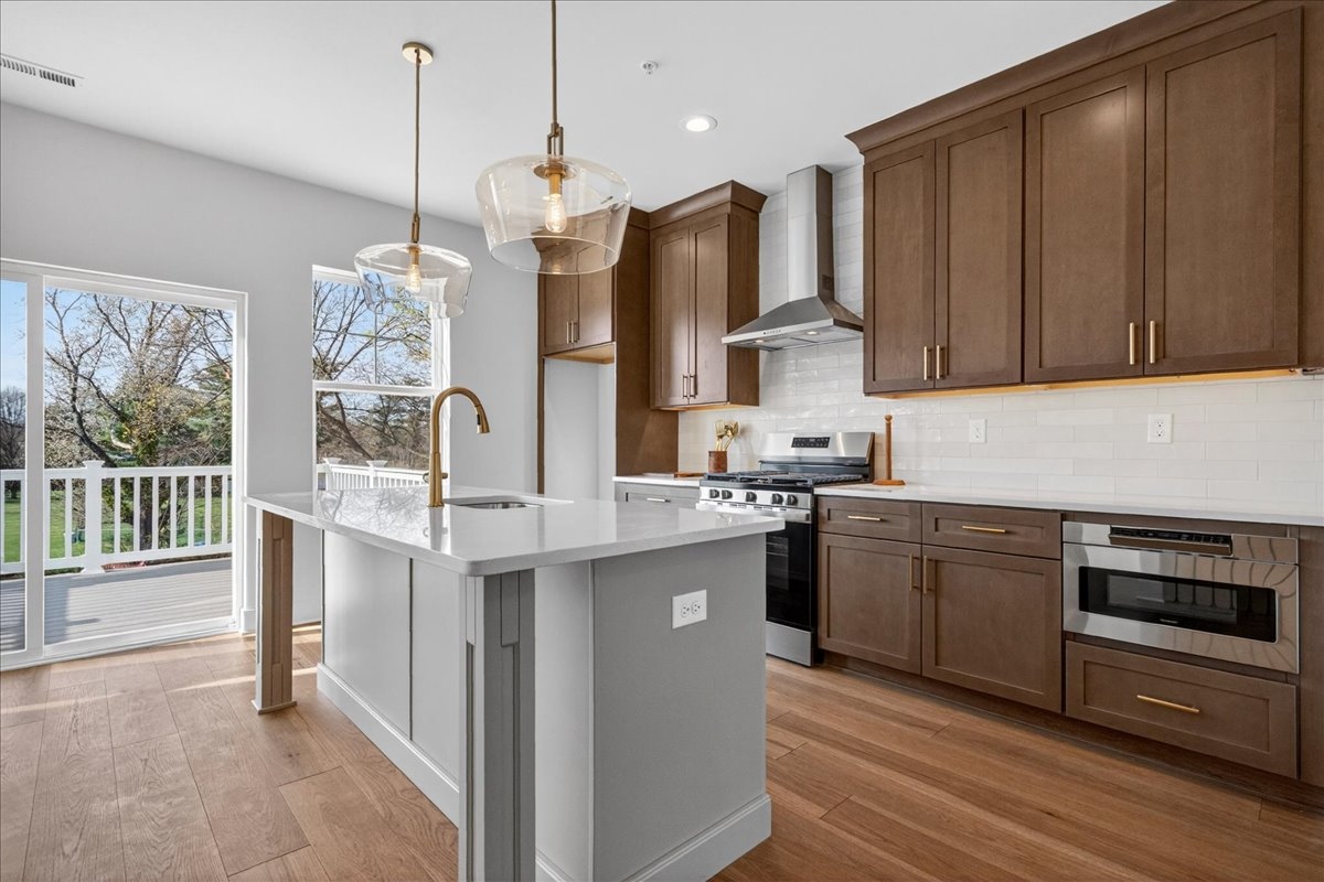 Kitchen with dark walnut shaker cabinets, white quartz counters, gold globe pendants, and a gas range with brass hardware