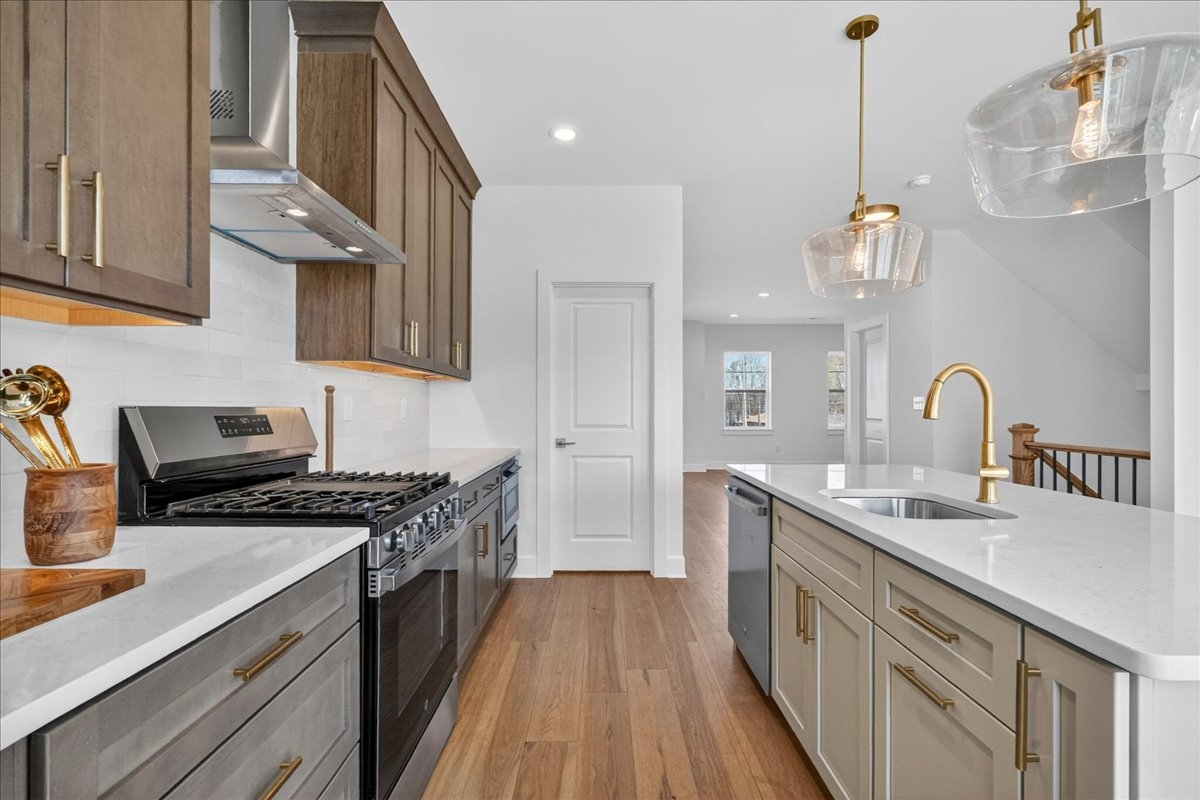 Kitchen alternate view showing wood-paneled hood, subway tile backsplash, stainless range, and an island with sink and gold faucet