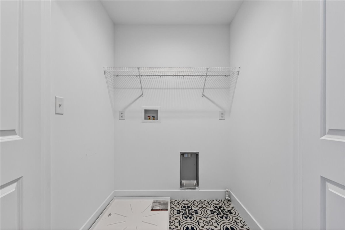 Upper-floor laundry room with washer and dryer hookups, patterned tile floor, and wire storage shelf