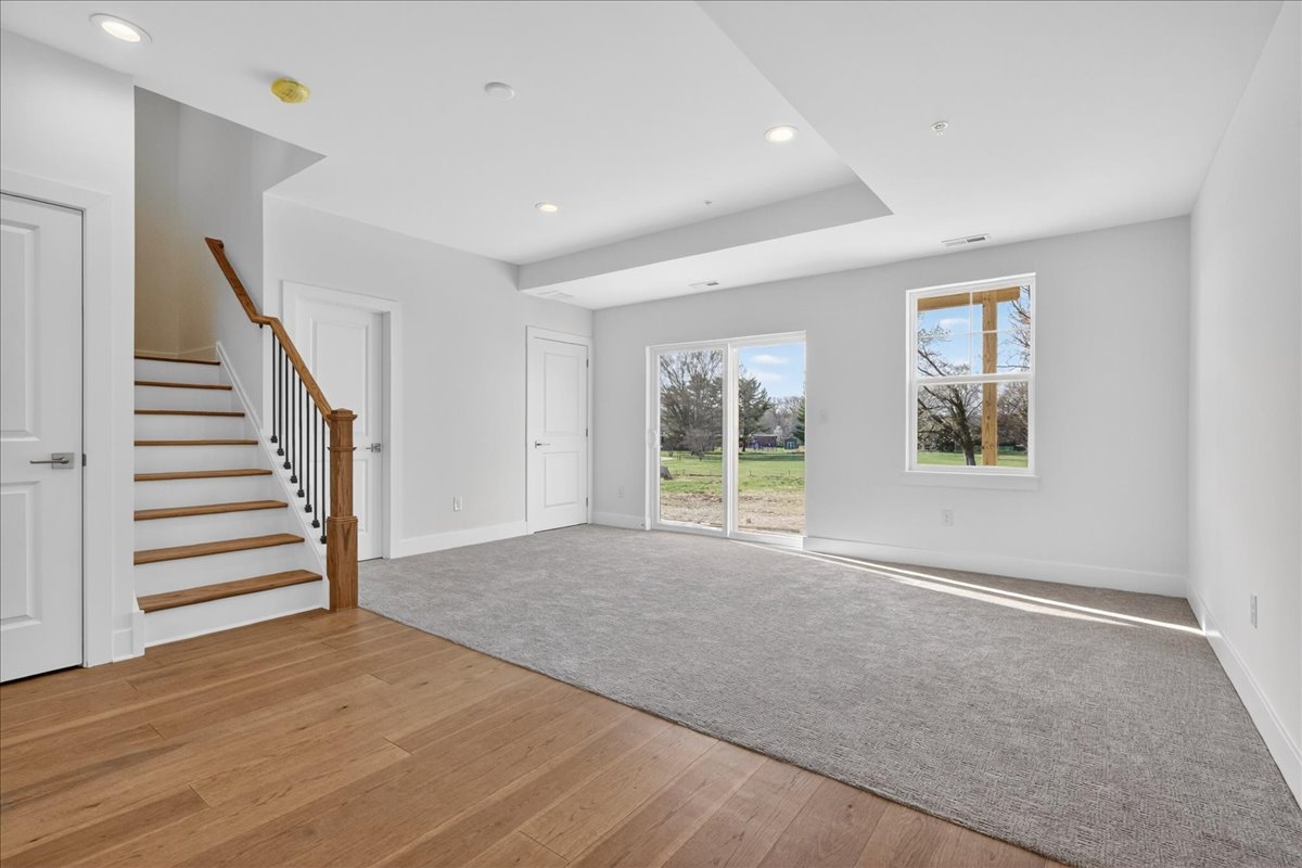 Open living area with hardwood floors, staircase with black metal spindles, and sliding door to the rear yard