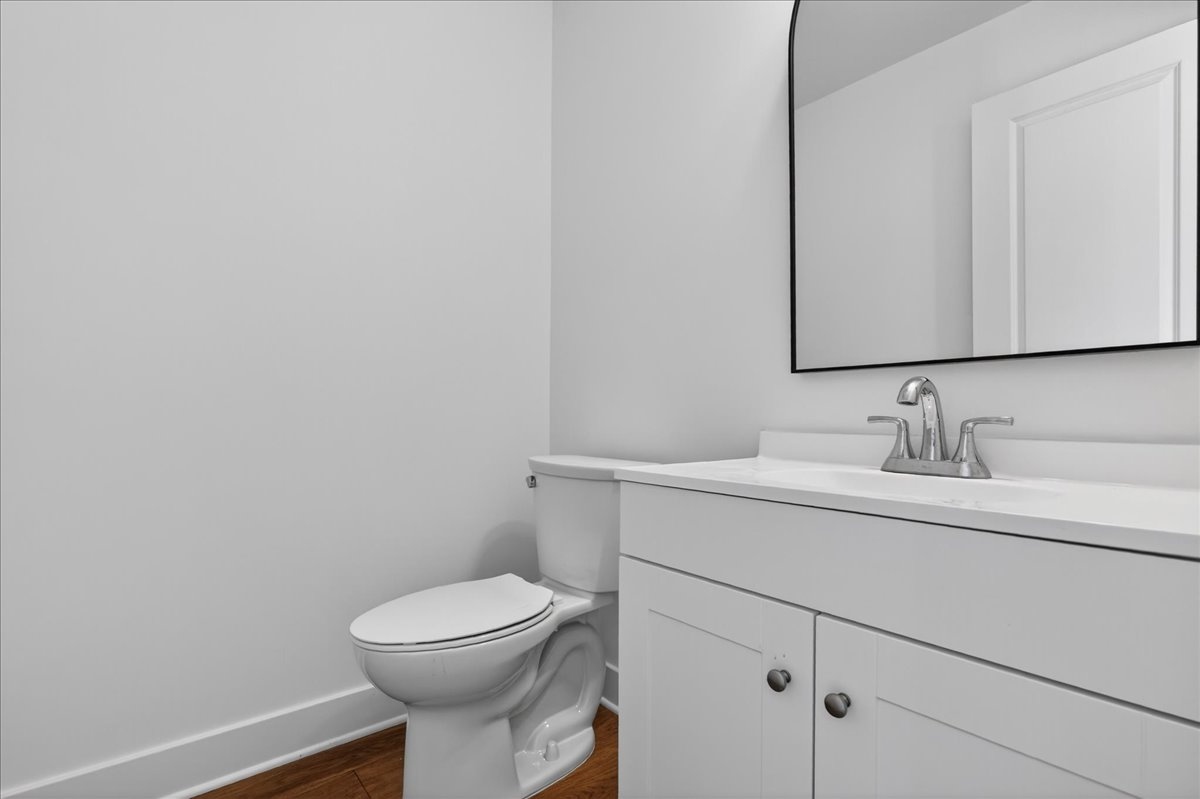 Powder room with a white shaker vanity, arched wood-framed mirror, and brass fixtures