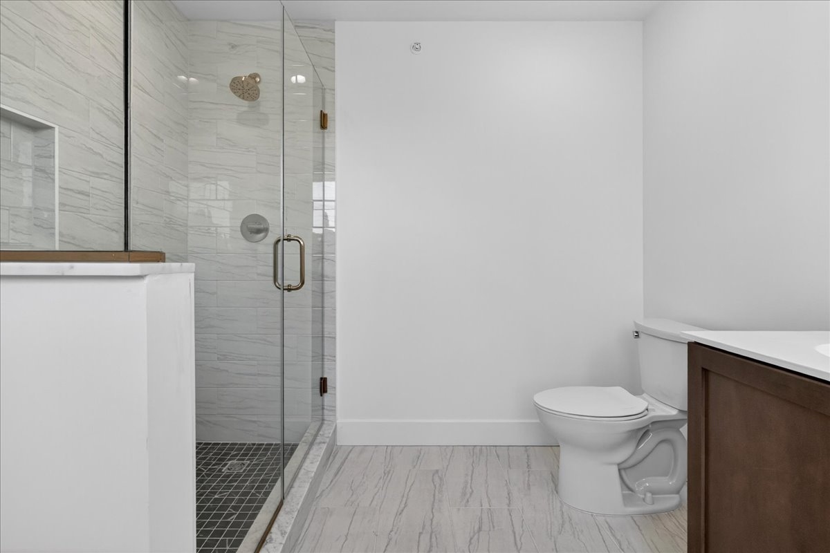 Primary bath frameless glass shower with marble-look tile, brass shower fixtures, and a shower niche